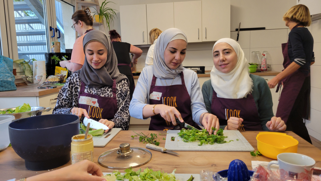 Drei Frauen sitzen nebeneinander am Tisch und schneiden Kräuter