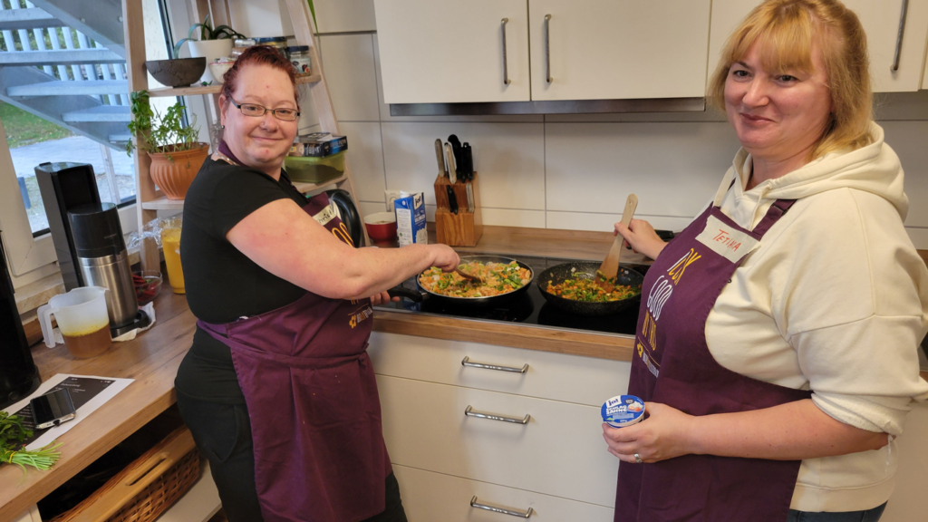 Zwei Frauen stehen am Herd und braten etwas in zwei Pfannen